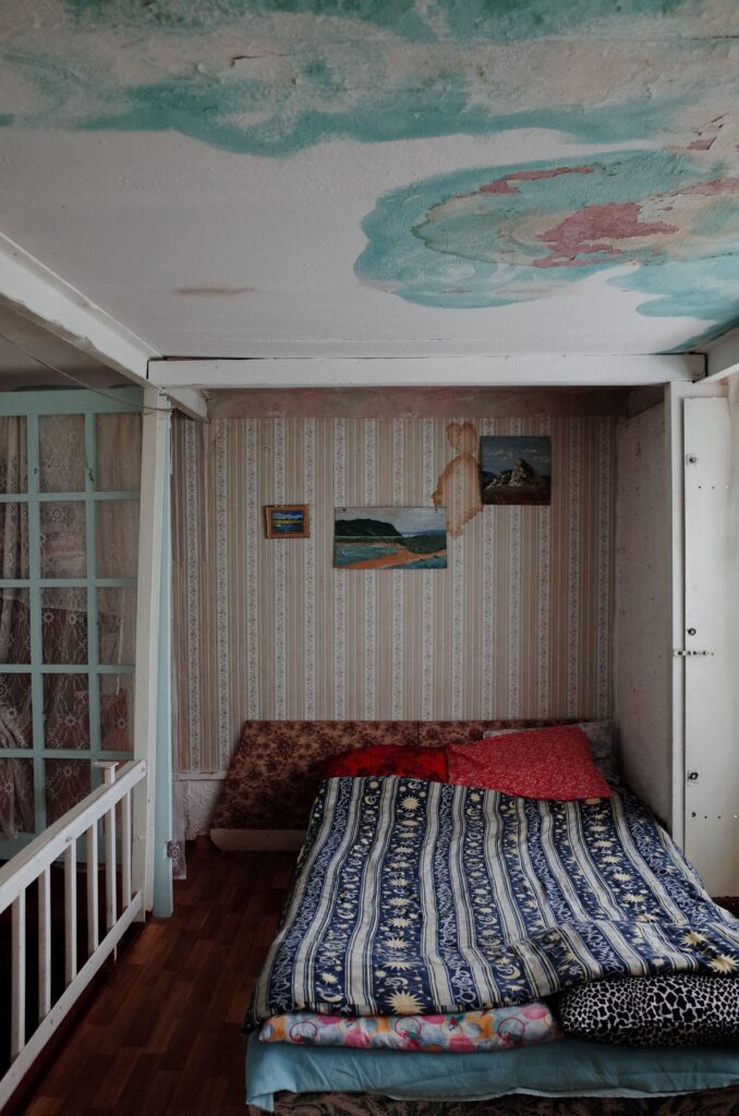Mould on a bedroom ceiling, a bed below against a water stained wall.